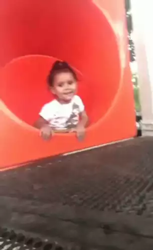 Toddler Waves Hello from Playground Slide